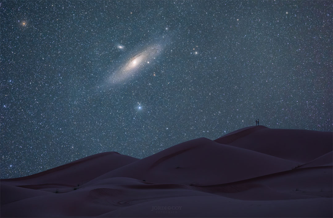 The featured image shows a zoom into the Andromeda Galaxy
over dunes in the Sahara Desert. Two people are barely visible 
at the top of one of the dunes.
Please see the explanation for more detailed information.