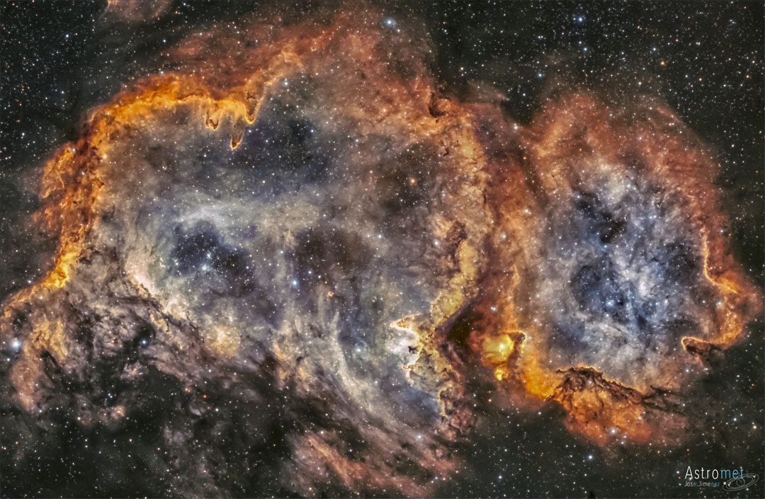 A red tinged nebula is shown in front of a starfield. 
Dust structures appear around the nebula's edge, and stars
are also seen near the nebula's center.
Please see the explanation for more detailed information.