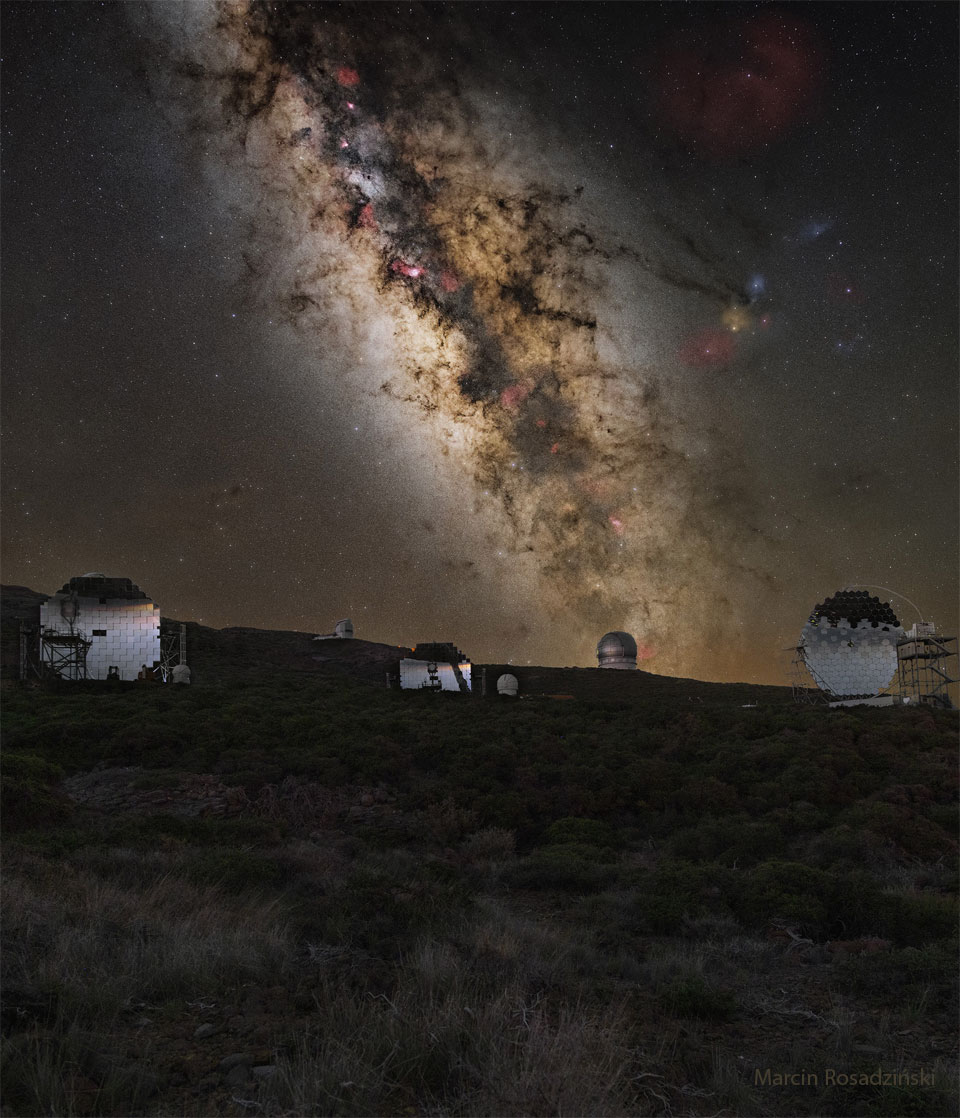 A mountaintop is shown covered by brush. Across the horizon are
several telescopes. Behind the mountaintop is a deep exposure of
the sky showing the central band of our Milky Way galaxy and several
well-known stars and nebulas.
Please see the explanation for more detailed information.