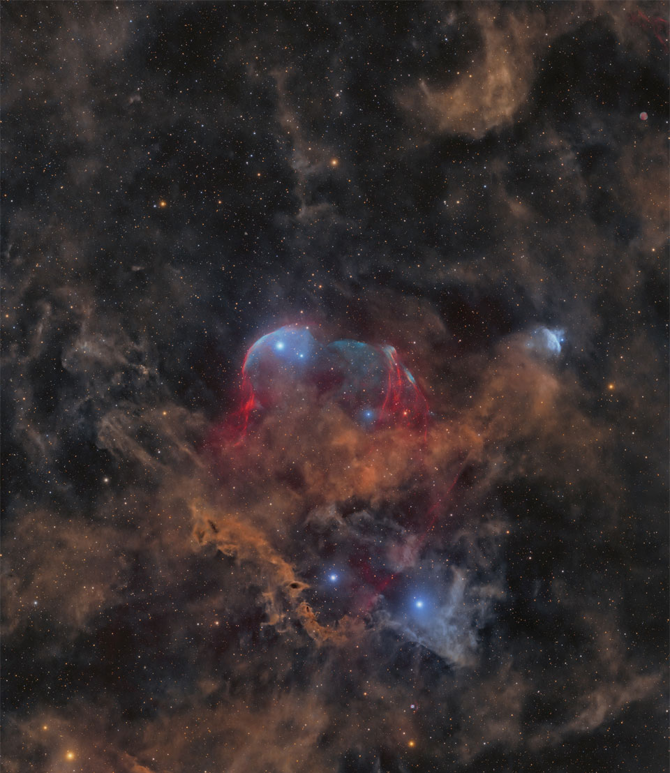 A starfield is shown with many stars and several faint
light brown dust clouds. In the center is a large cloud with
brown dust and gas shells lined in blue. 
Please see the explanation for more detailed information.