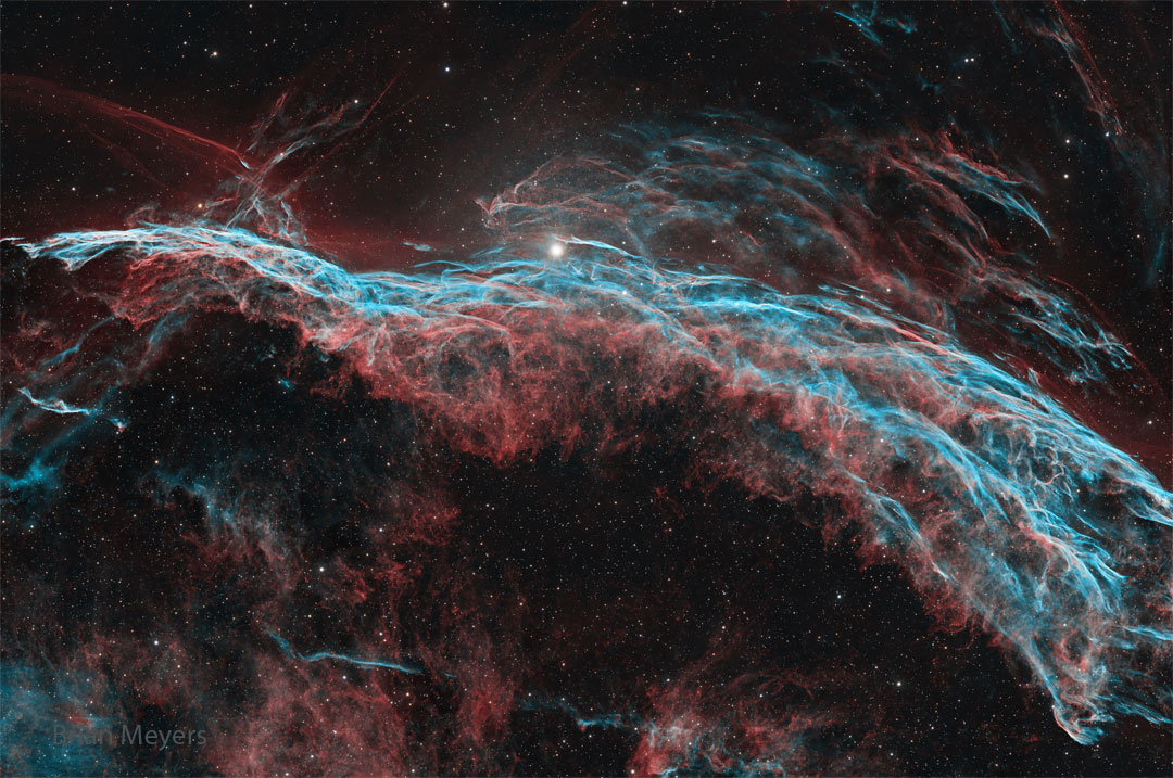 A starfield is shown that has a multi-filament
nebula flowing across it horizontally. The most 
prominent colors are red and blue. 
Please see the explanation for more detailed information.