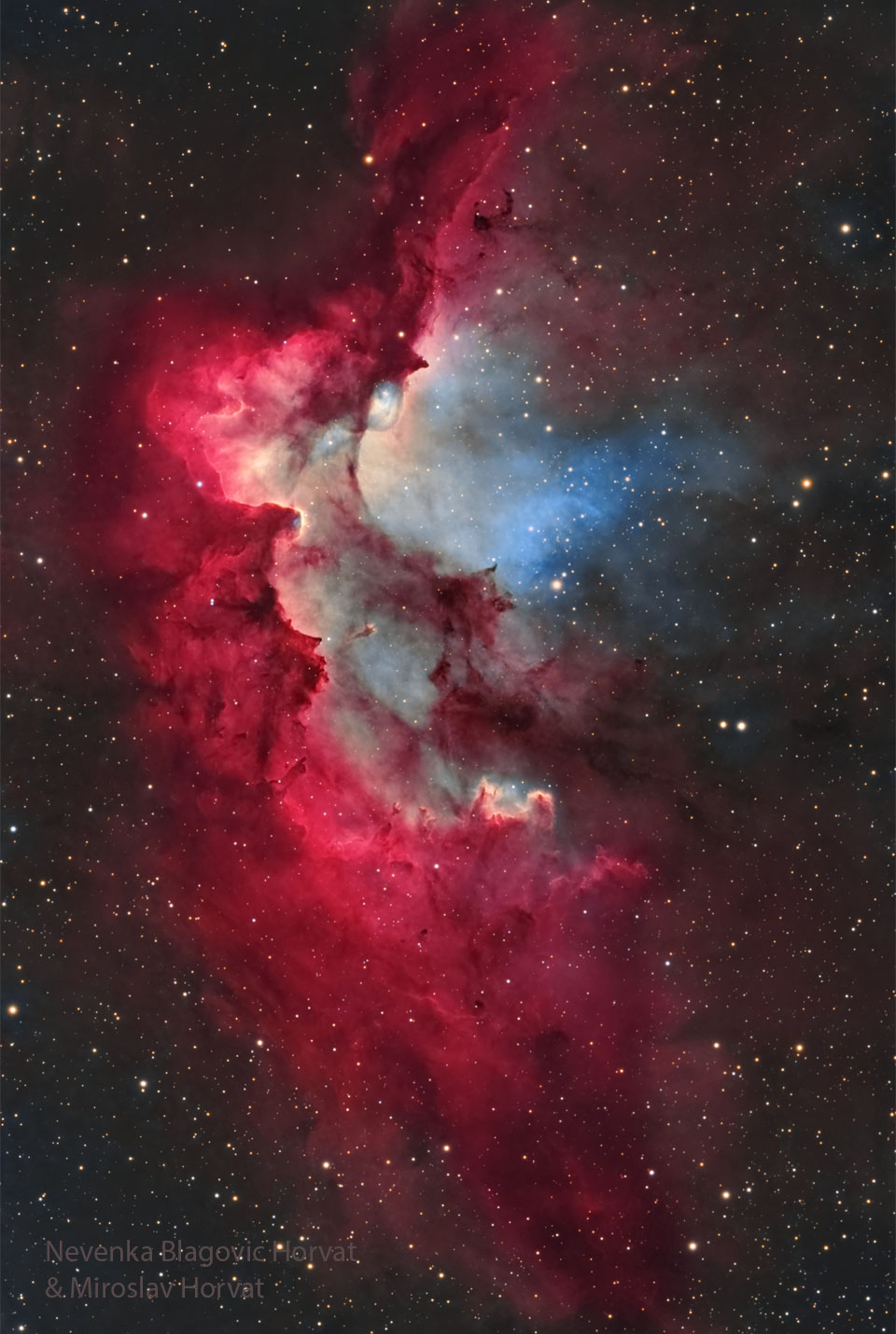 A starfield is shown surrounding a bright gaseous 
nebula in red with bits of white and blue. Pillars of 
dust and gas appear around the interior of the nebula
pointing to energetic stars in a cluster in the nebula. 
Please see the explanation for more detailed information.