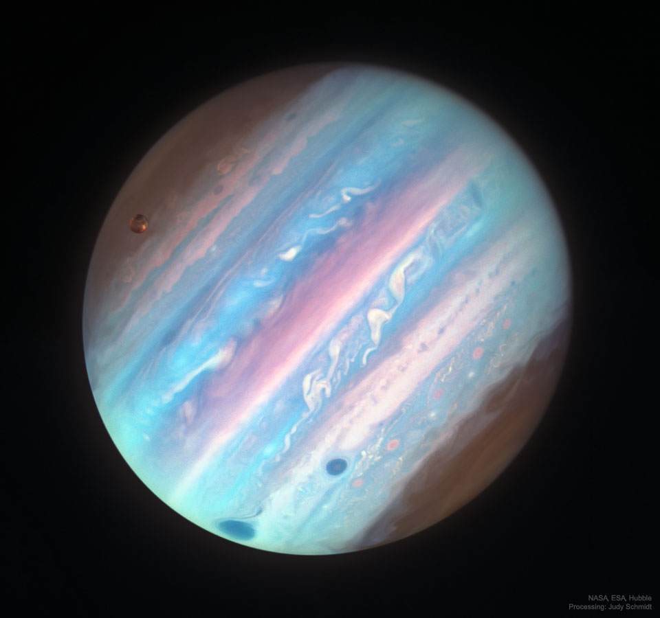 The planet Jupiter appears full frame in apparent colors 
of a variety of blues and some pink bands. The Great Red Spot
is visible on the lower left as a dark spot. Jupiter's Moon
Ganymede is visible on the upper left. 
Please see the explanation for more detailed information.