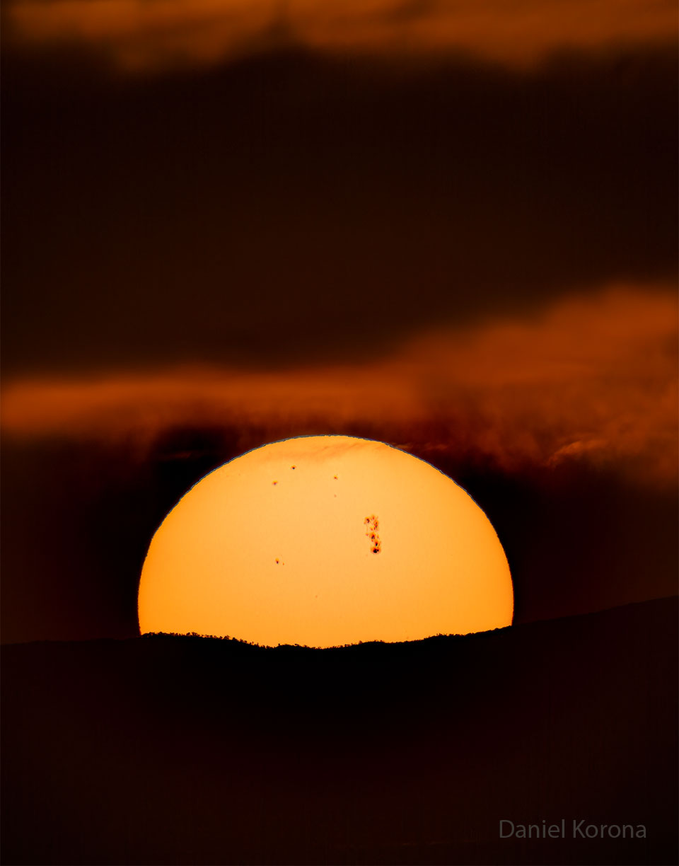 Most of the Sun is pictured peeking over a hill.
On the surface of the Sun are several sunspots including 
a very large sunspot region toward the center-right.
Please see the explanation for more detailed information.