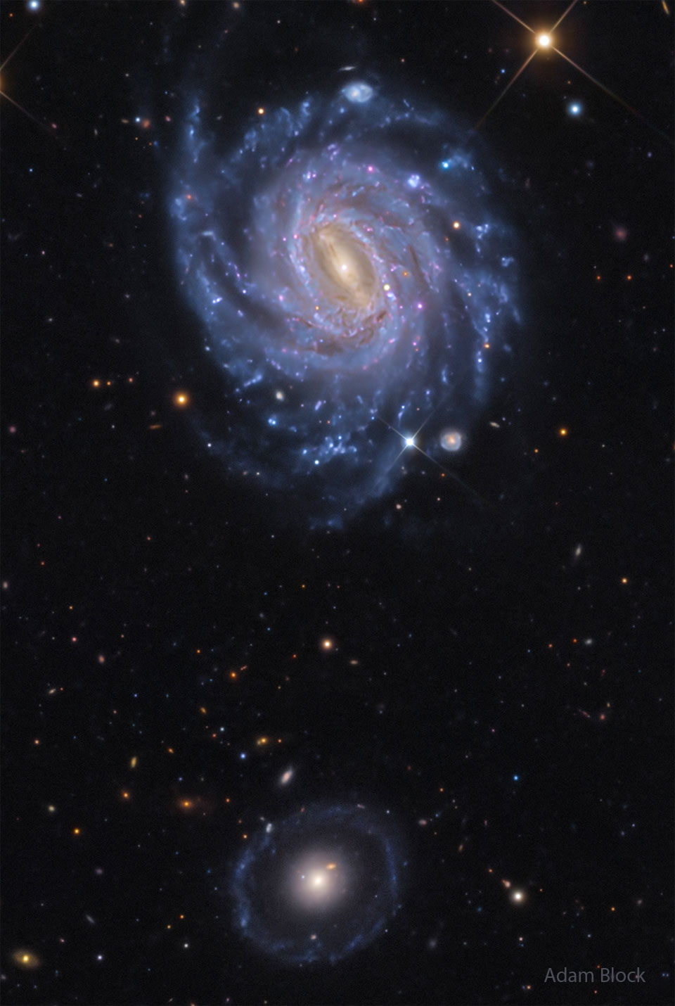 A starfield is shown showing two prominent galaxies. 
Near the top is a bright spiral galaxy with several blue
spiral arms. Near the bottom is a fainter circular 
galaxy with a bright center. 
Please see the explanation for more detailed information.