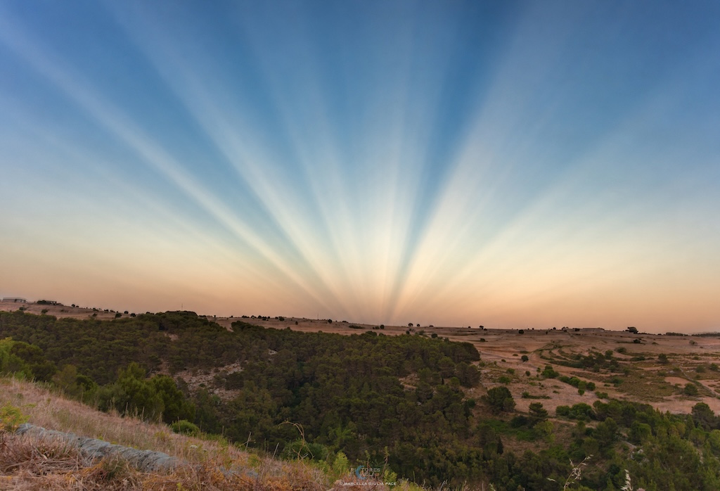 A landscape with an open horizon shows
	    sunset color and coverging rays of light.